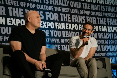 Vincent D'Onofrio sitting on a couch next to Charlie Cox holding a microphone talking on a panel