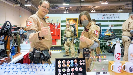 Two exhibitors are dressed in ghostbusters costumes and are standing at their booth