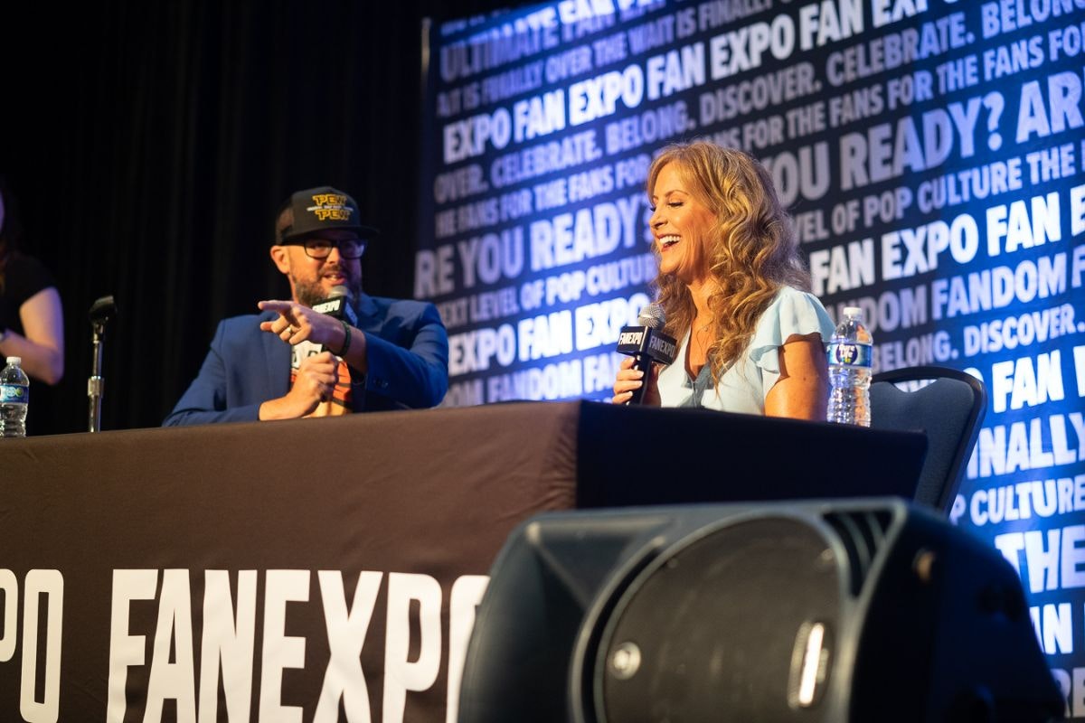 JODI BENSON SITTING AT A TABLE WITH A MICROPHONE WITH A MODERATOR SITTING NEXT TO HER