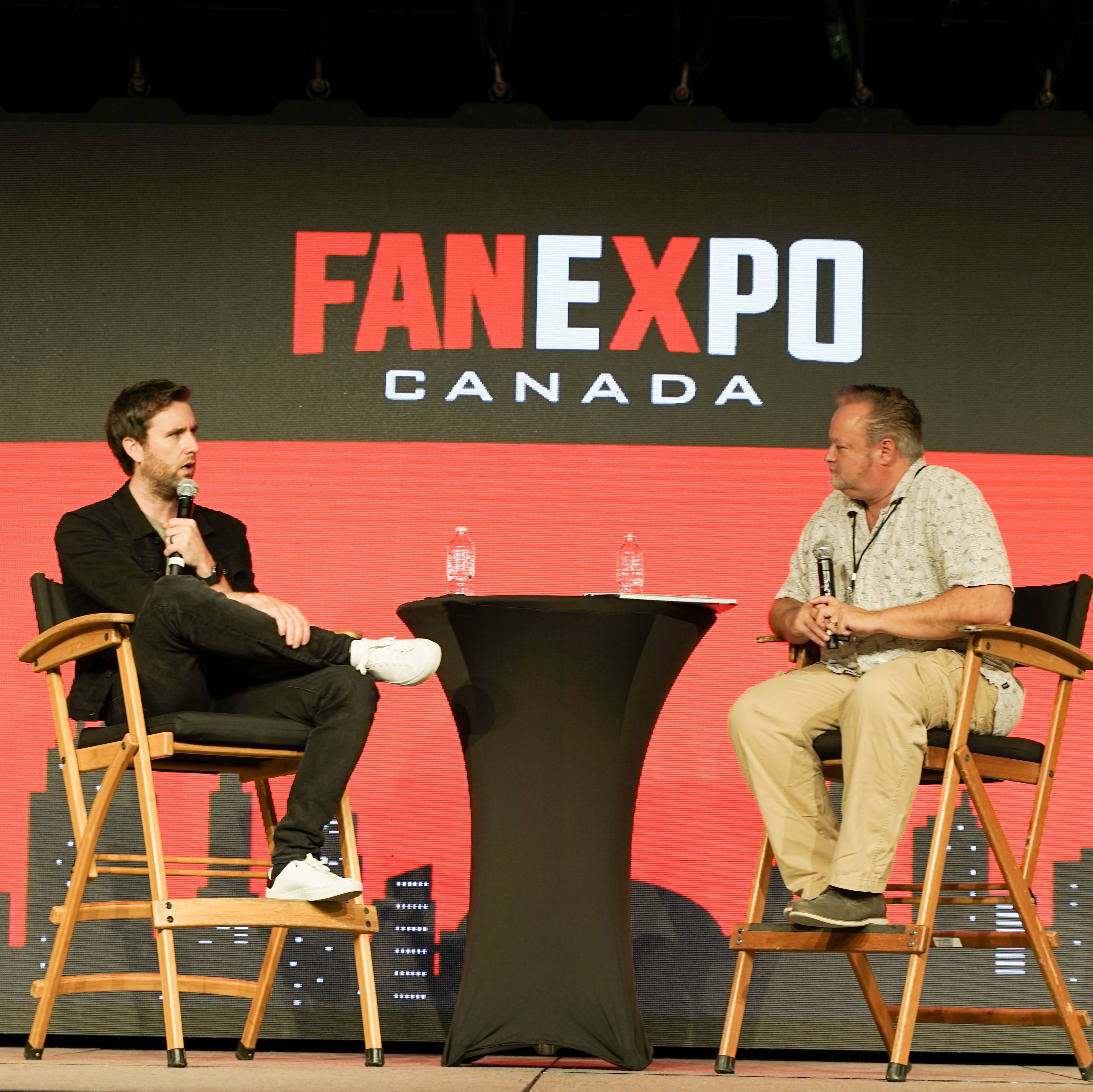 He is sitting on a panel with the FAN EXPO Canada in the background. It looks like he is answering a question.
