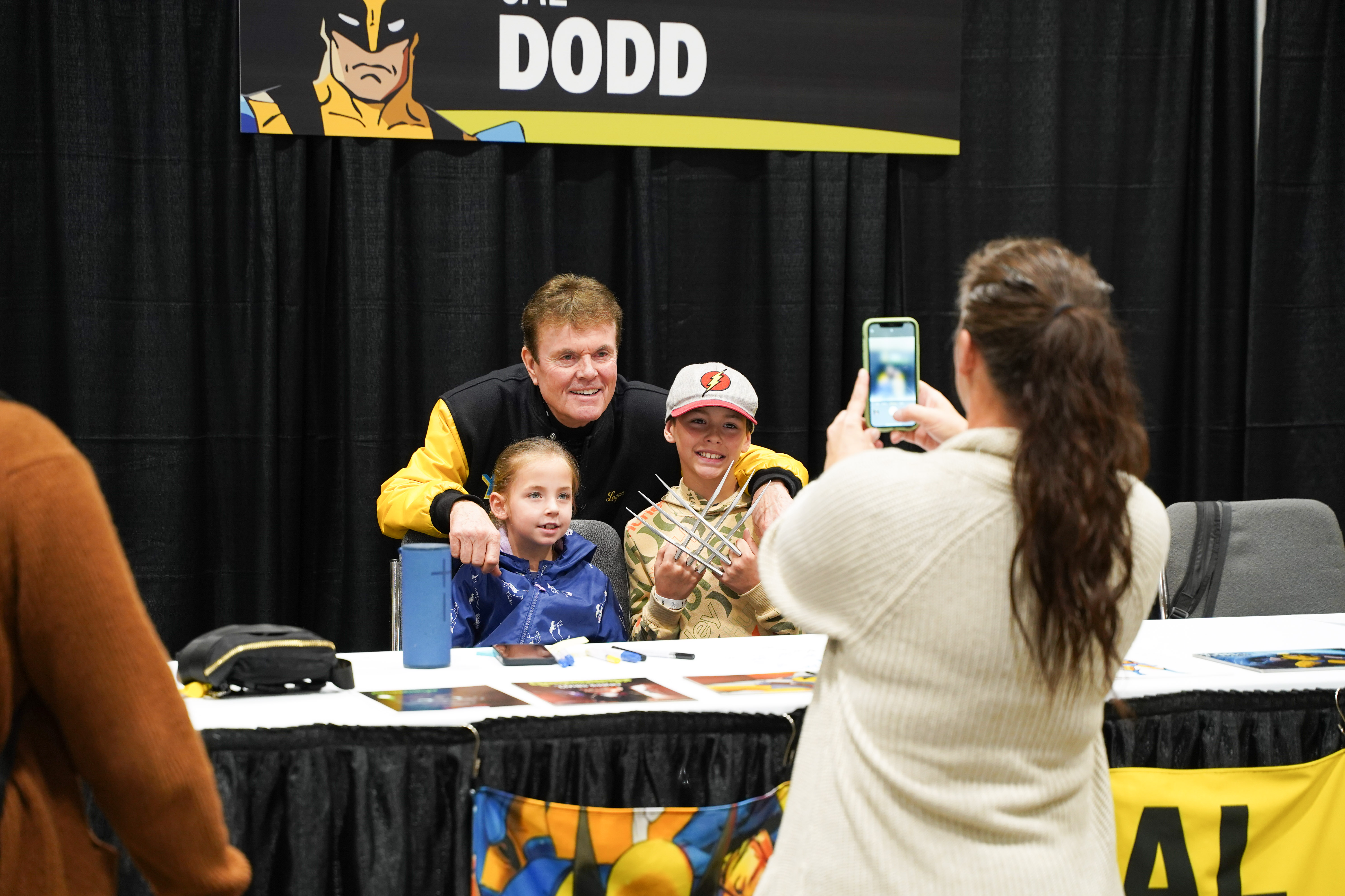 CAL DODD, VOICE OF WOLVERINE, TAKES A PHOTO WITH TWO YOUNG FANS AS THEIR PARENT TAKES A PHOTO - YOUNG BOY, LEFT, IS WEARING WOLVERINE CLAWS FOR THE PHOTO