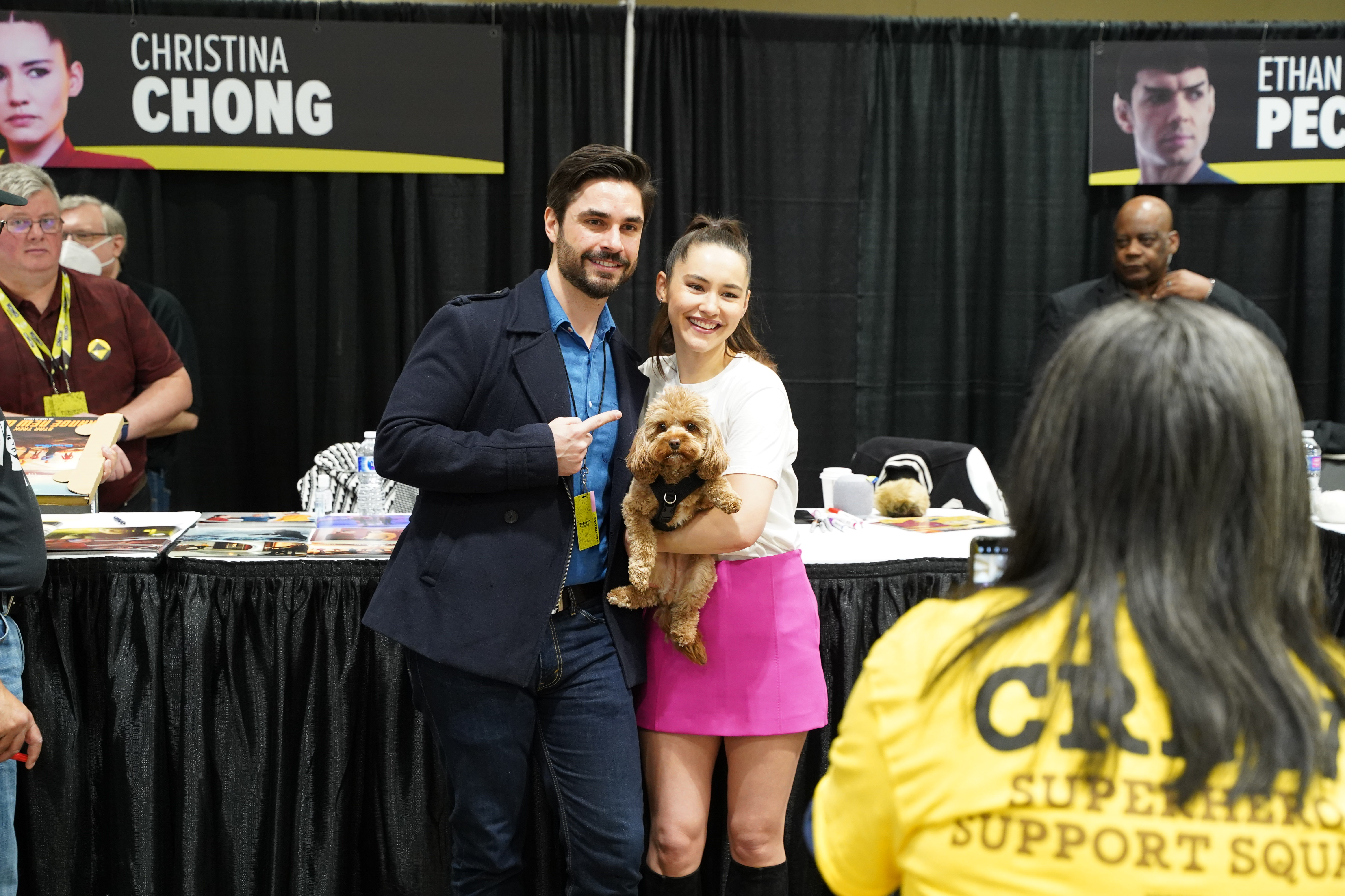 CHRISTINA CHONG POSES FOR A PHOTO WITH A FAN, HOLDING HER BELOVED PUP RUNA BETWEEN THEM AS A CREW MEMEBER TAKES THE PHOTO.