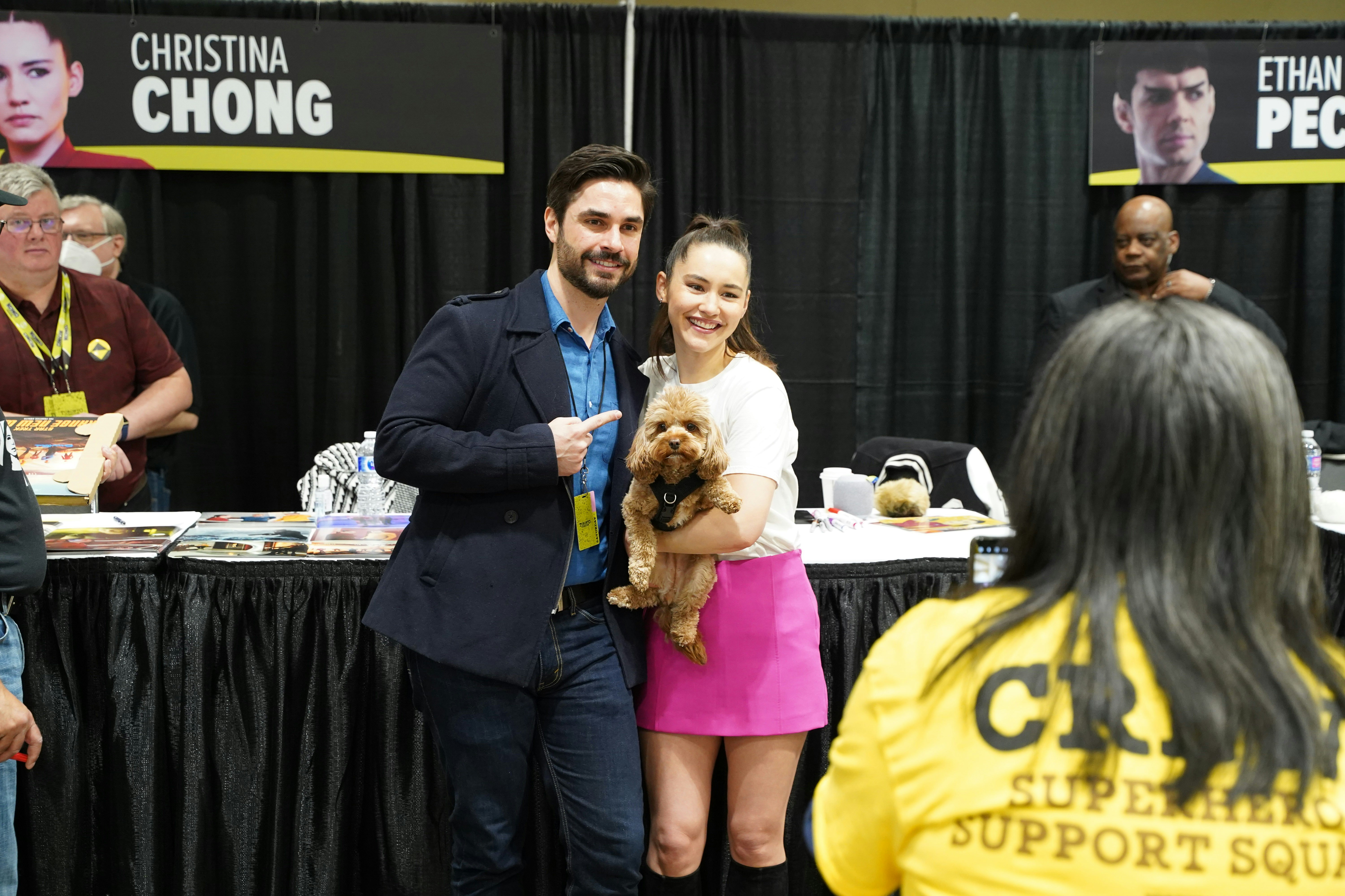 CHRISTINA CHONG POSES FOR A PHOTO WITH A FAN, HOLDING HER BELOVED PUP RUNA BETWEEN THEM AS A CREW MEMEBER TAKES THE PHOTO.