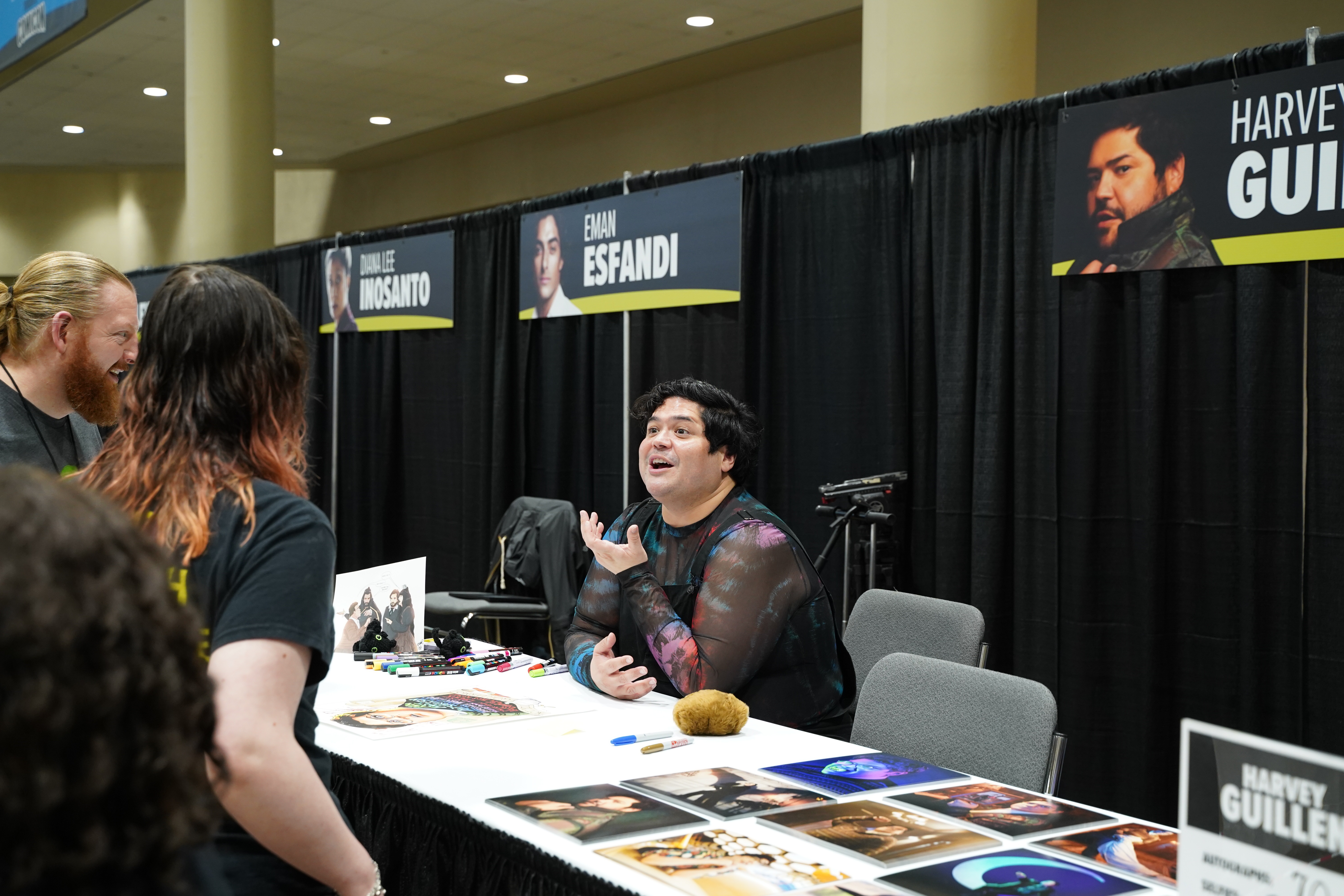 Harvey Guillen, seated behind his table, speaks excitedly to fans who have approached to meet him.