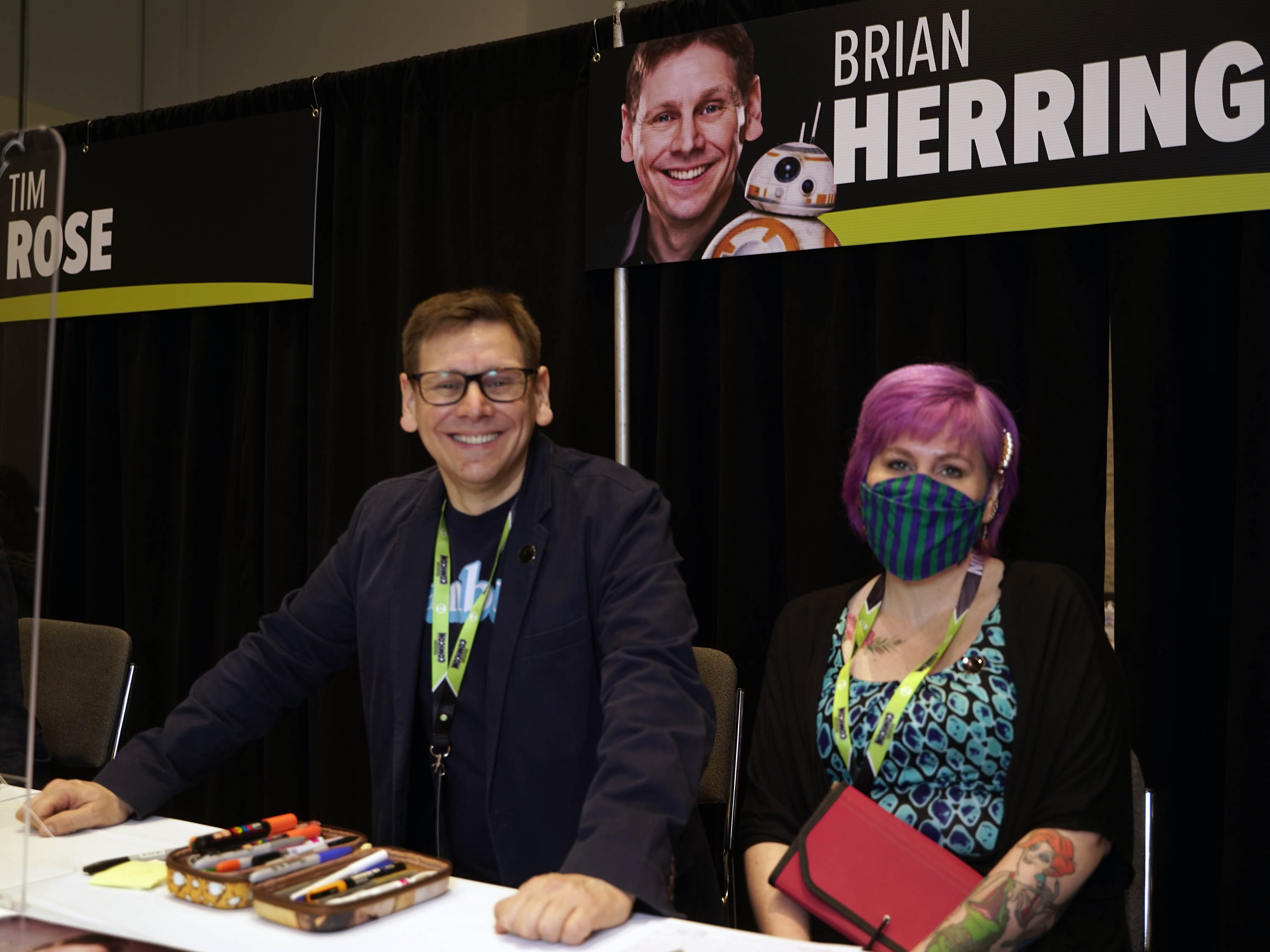BRIAN HERRING and his agent posing at his autograph table underneath a banner with BB8 on it