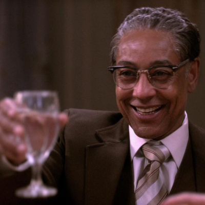 Giancarlo in a brown suit, smiling, and lifting a drinking glass.
