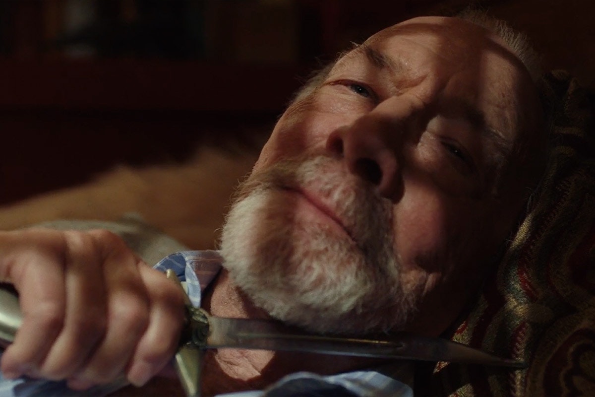 Harlan Thrombey holding a knife to his own throat