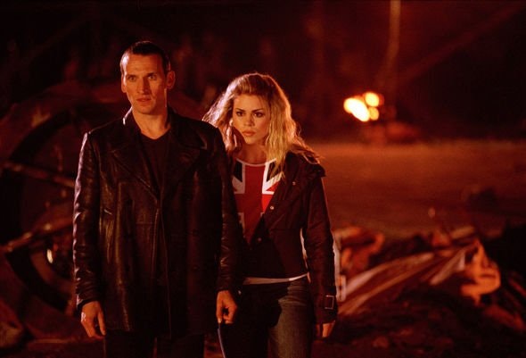 Fire rages in the distance; Rose and the Doctor stare on in concern amongst a pile of metal and other various forms of rubble and debris.