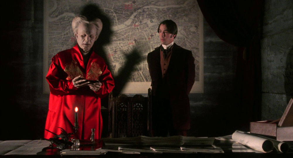 Dracula and Harker stand in Dracula's study, in front of a large map, marked in various places. Dracula is deep in conversation.