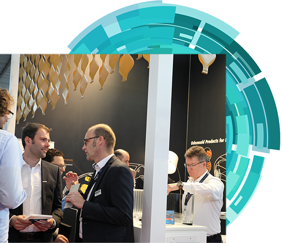 Attendees at an exhibition standing around a table, participating in conversation and sharing ideas