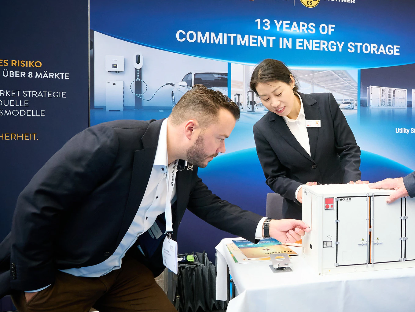 A man and woman pose next to a table featuring a box, smiling and engaging with the viewer.