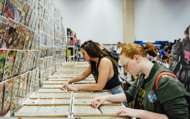 Two women sifting through boxes of comic books.