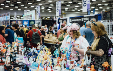 Two women looking at a table selling Anime-Themed small statues.