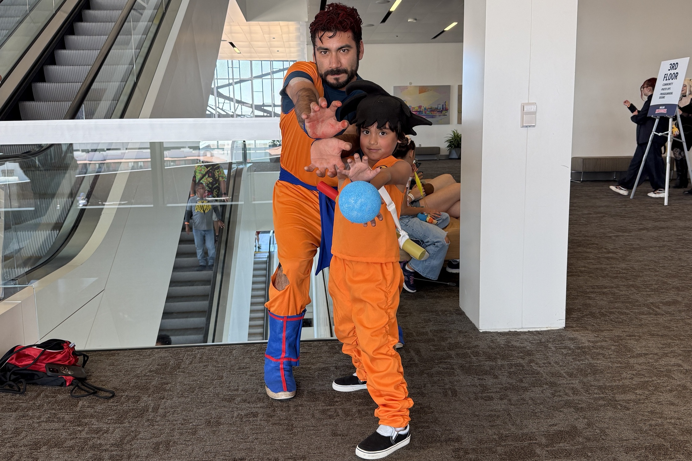 A father and son dressed as Goku from Dragon Ball Z strike a Kamehameha pose together inside the convention center.