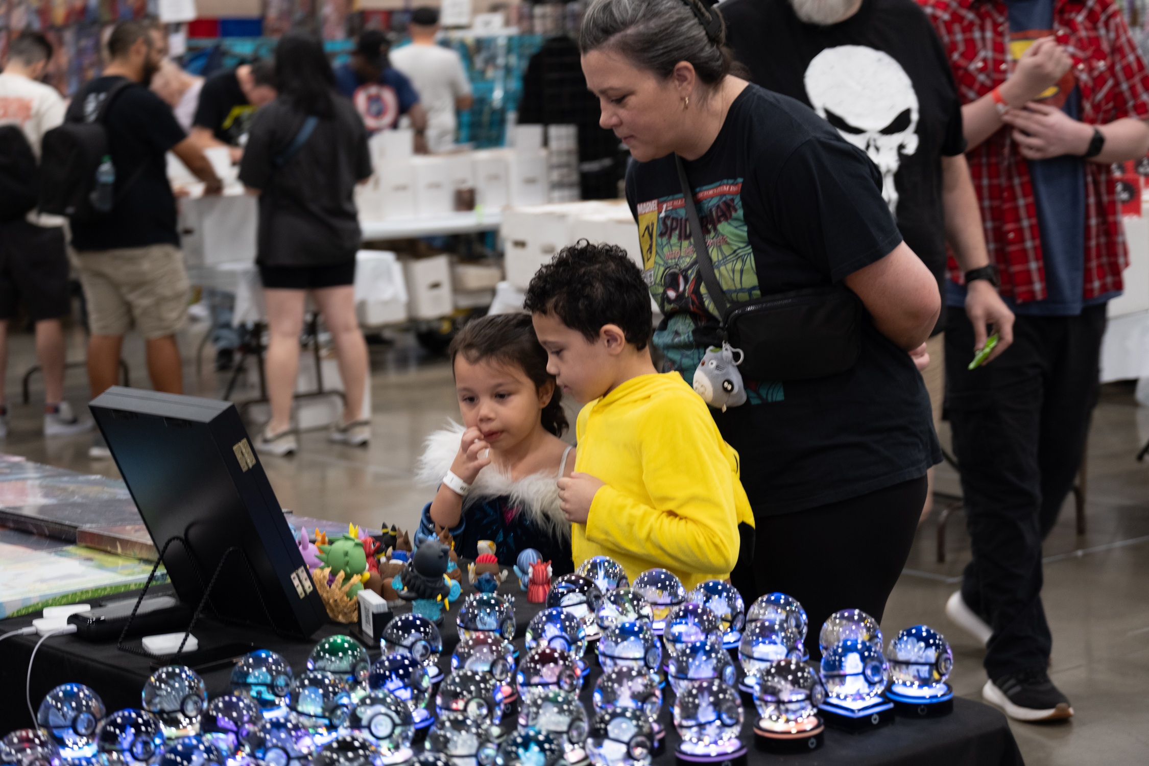 A woman and two children admire a vendor’s display of light-up crystal spheres and collectible figures on the show floor at FAN EXPO Dallas.