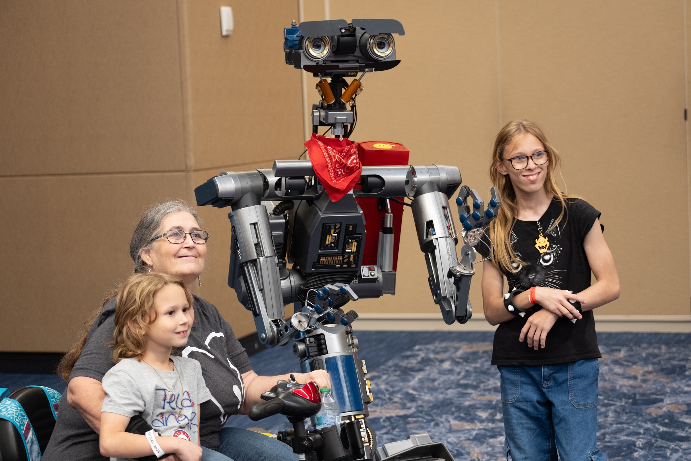 A grandmother and two kids smile beside a life-sized replica of Johnny 5 from Short Circuit inside the convention hall.