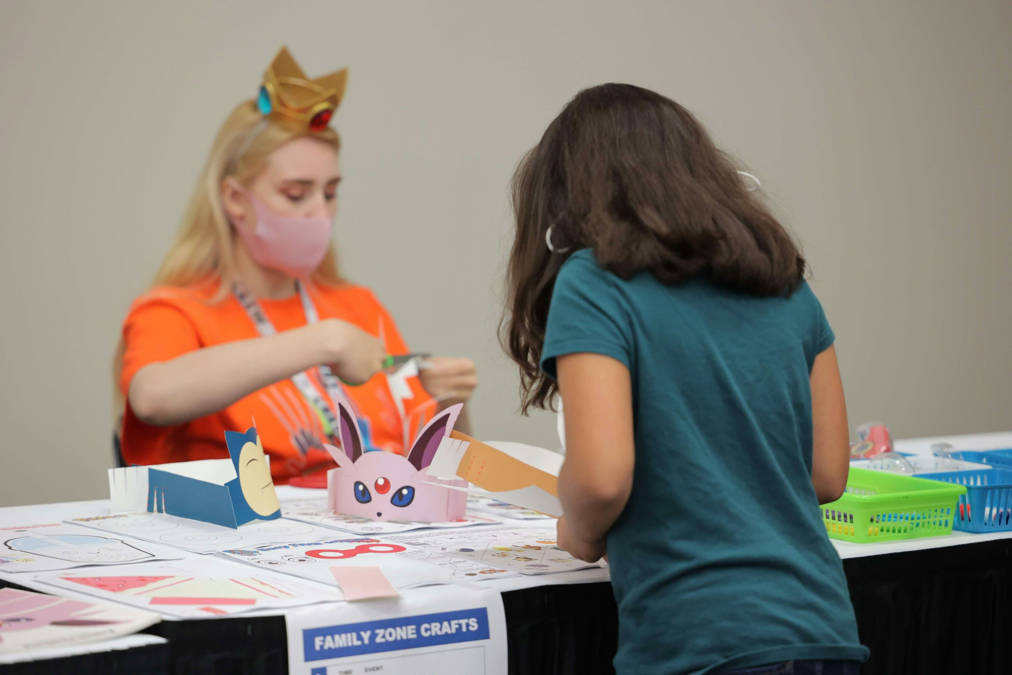 A volunteer in an orange shirt helps a child make a Snorlax head band to wear