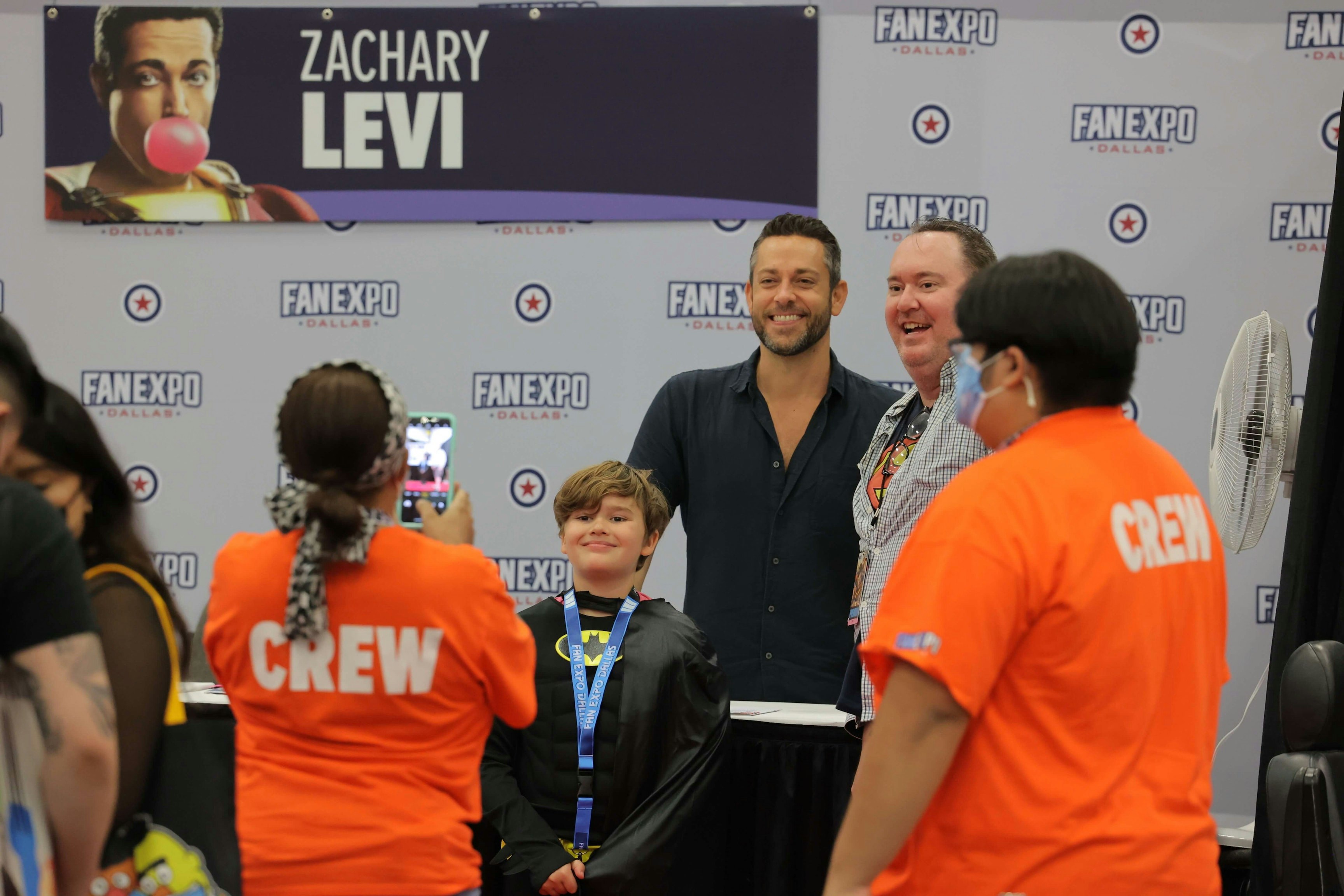 Zachary Levi takes a photo with a two fans at his autograph table