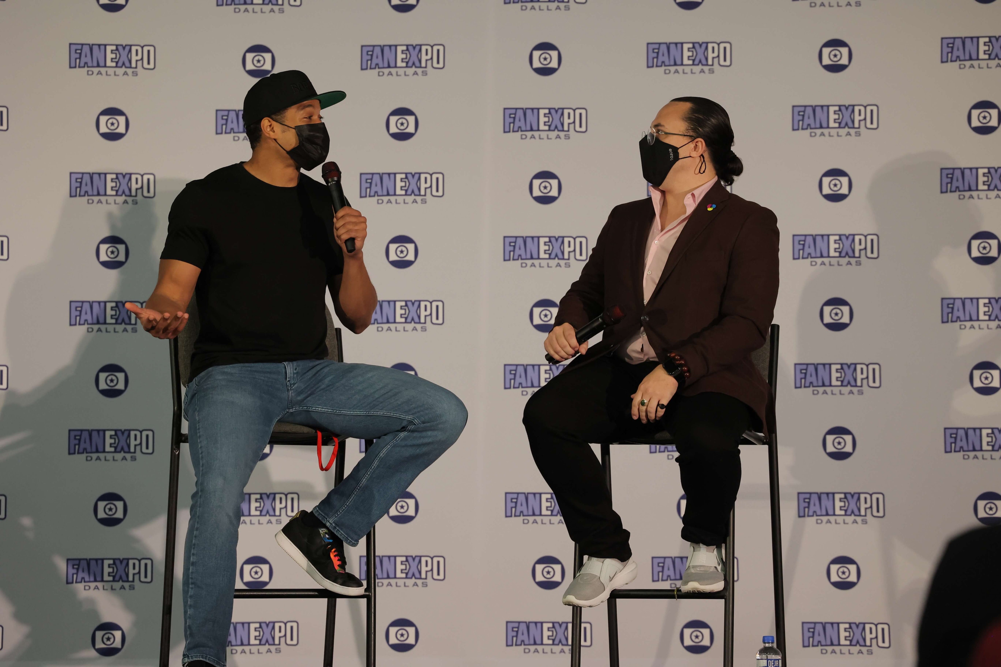 Ray Fisher sits on a chair on stage and speaks to the moderator of his panel