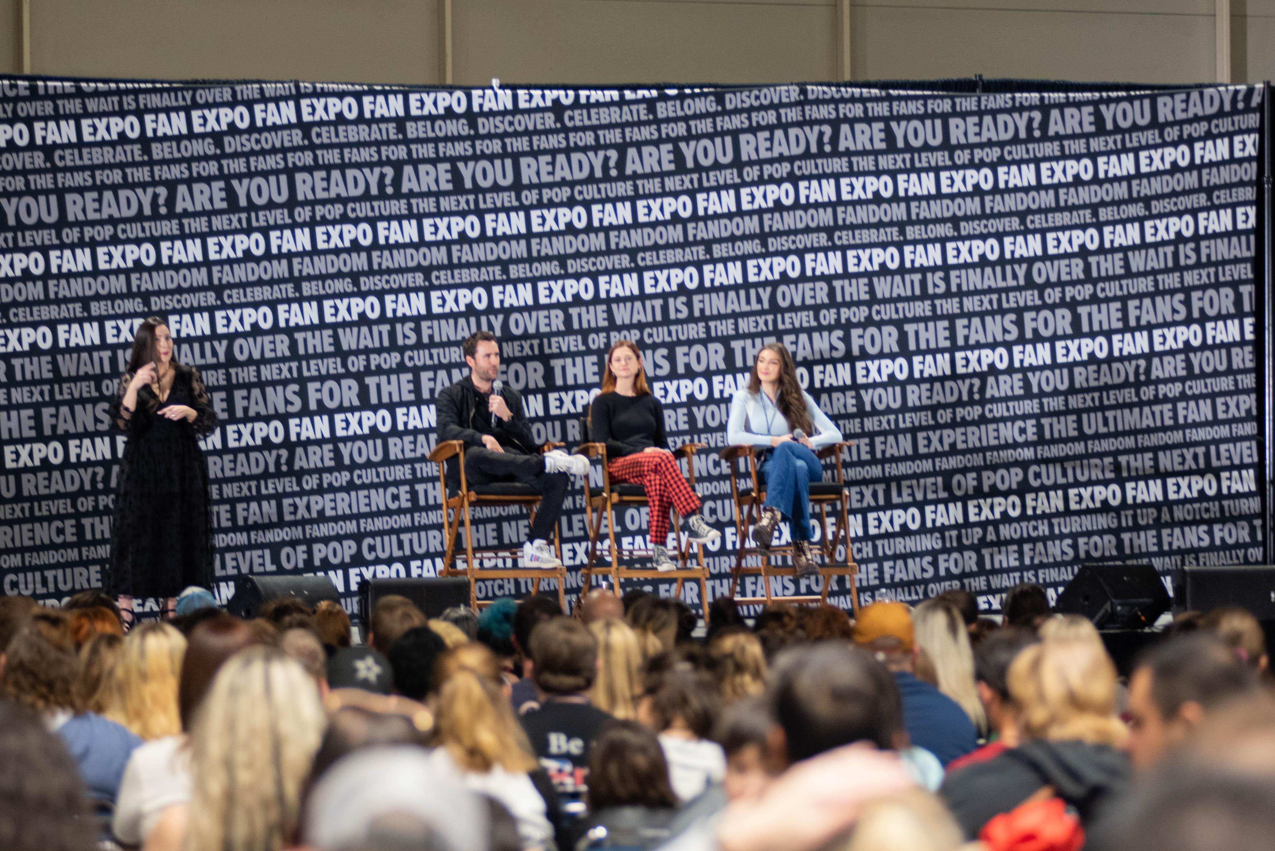 Matthew Lewis speaking at the Harry Potter panel as fellow star Bonnie Wright and the rest of the audience listen.