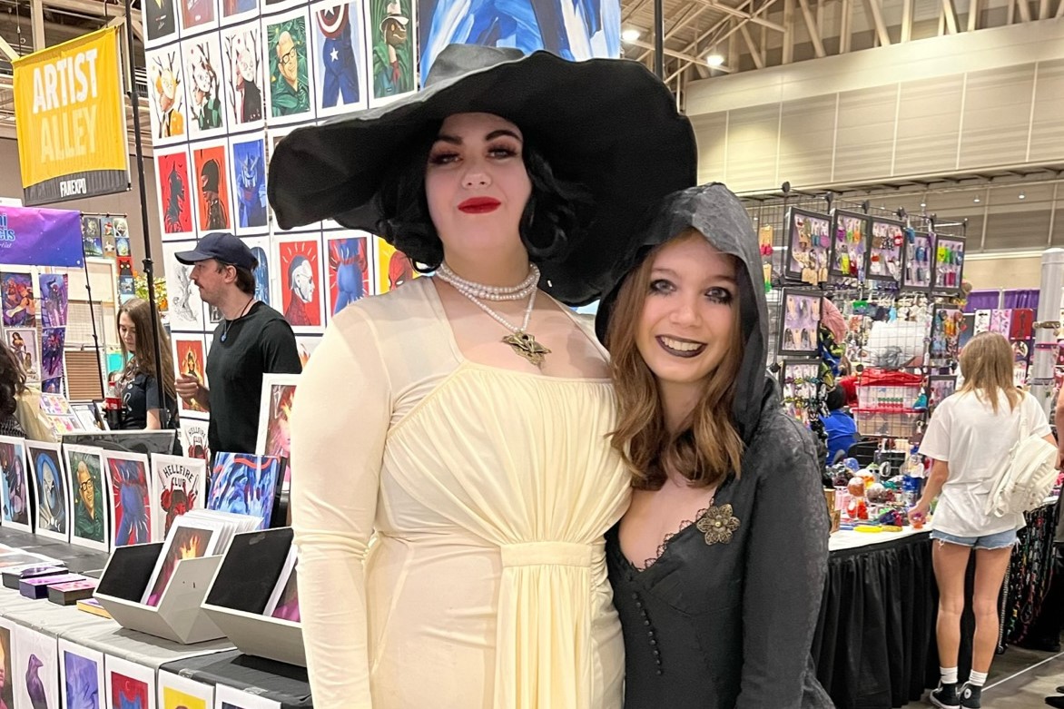 Two cosplayers, cosplaying as Lady Dimitrescu and Bela Dimitrescu from Resident Evil Village, smiling for the camera.