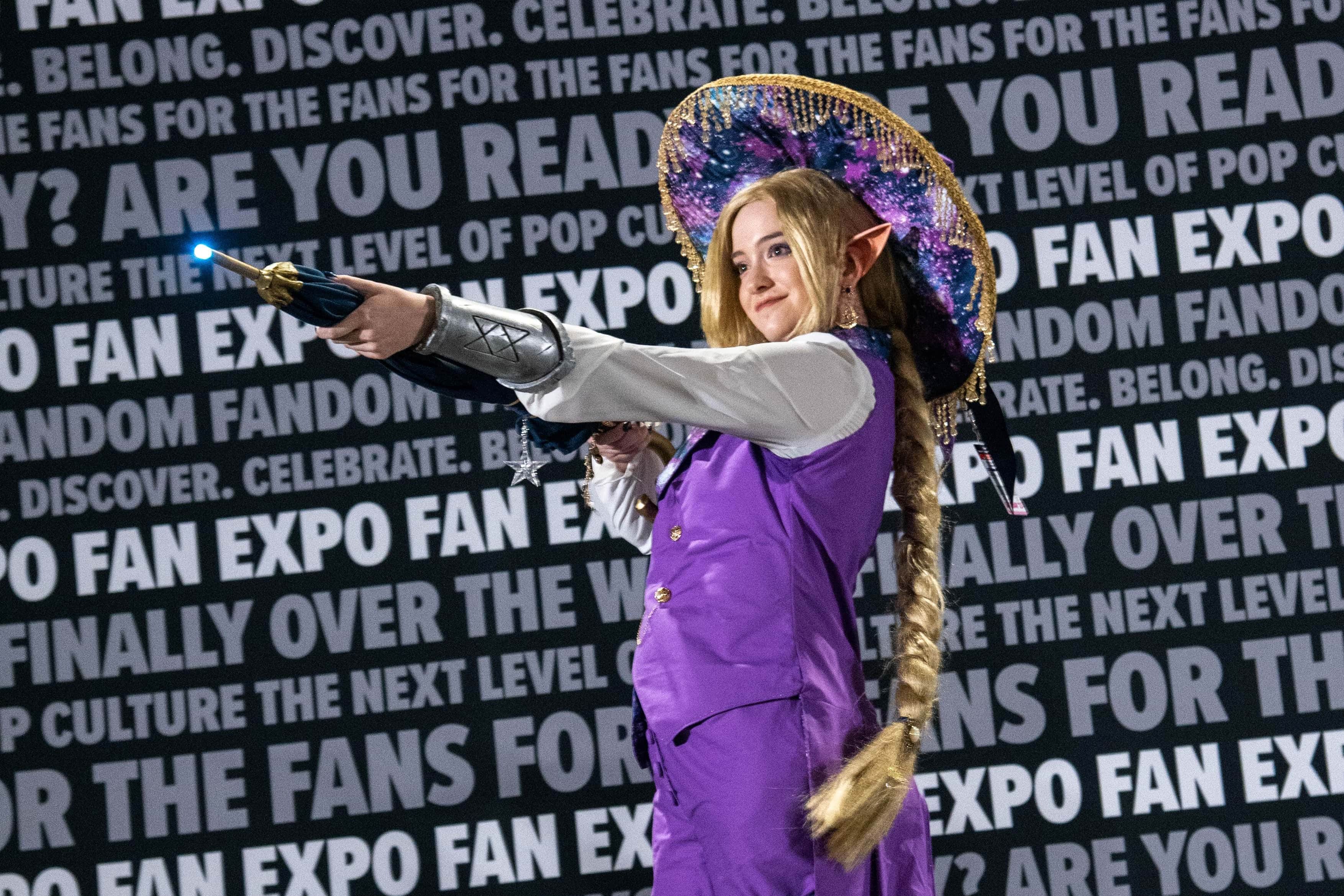 One of the Cosplay Craftsmanship Cup contestants on stage, aiming their prop umbrella at the crowd.