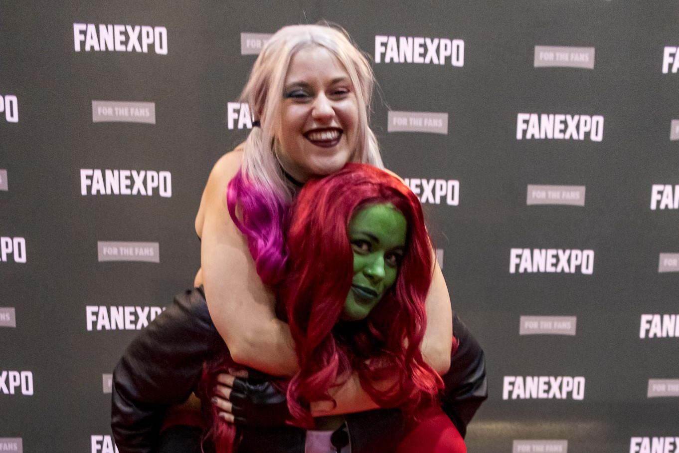 A Poison Ivy cosplayer carrying a Harley Quinn cosplayer on her back.