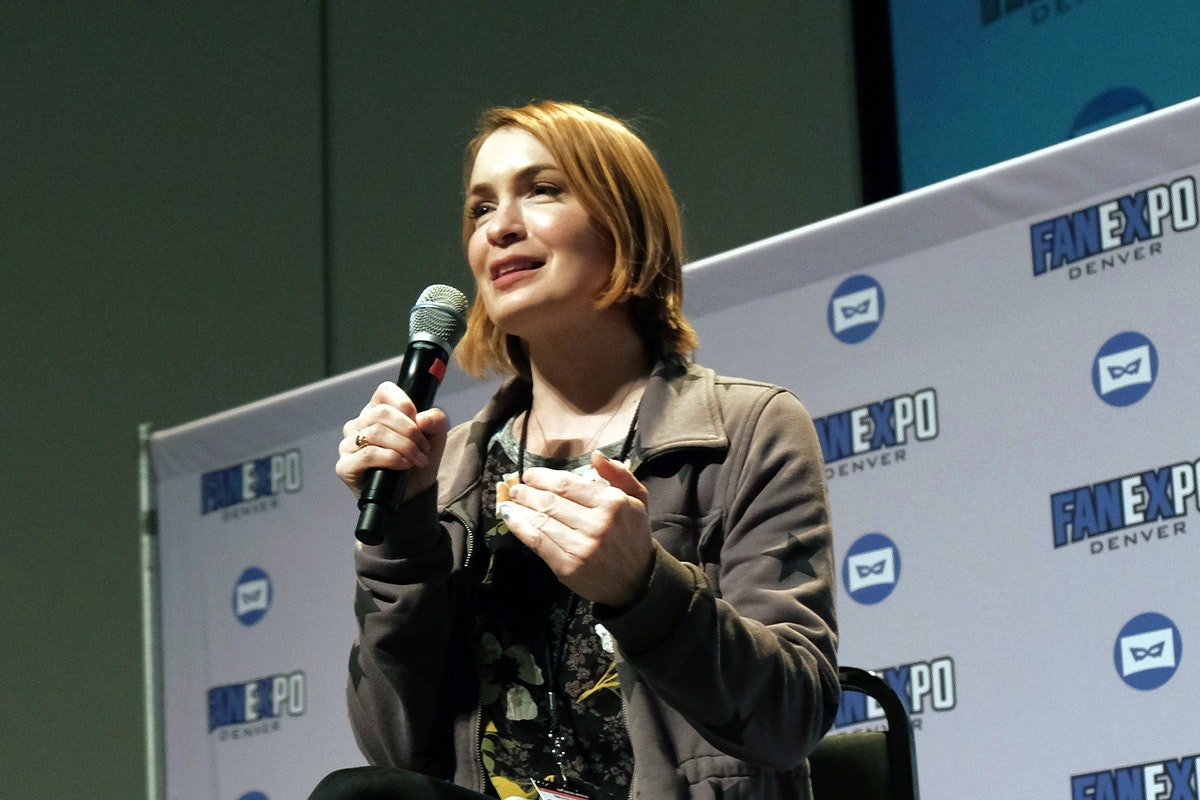 Felicia Day smiles as she answers a question on stage while holding a microphone
