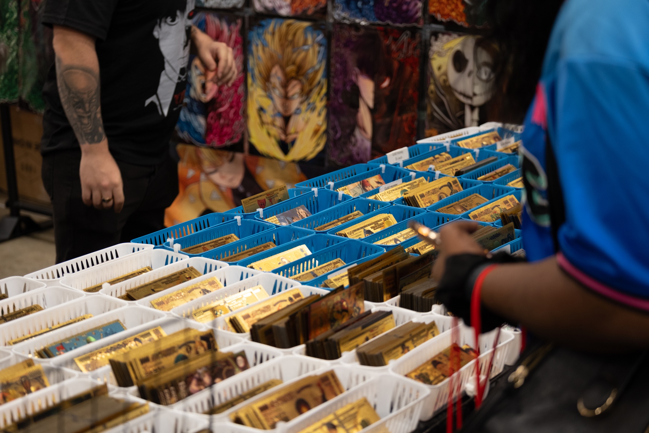 A fan browses through bins filled with shiny gold collectible bills featuring designs from popular fandoms at a vendor booth.