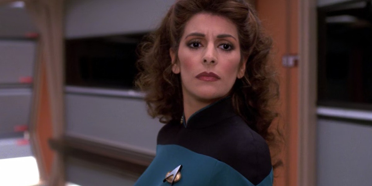 Deanna Troi stares off behind a colleague, off screen, in the control room on the Starship enterprise