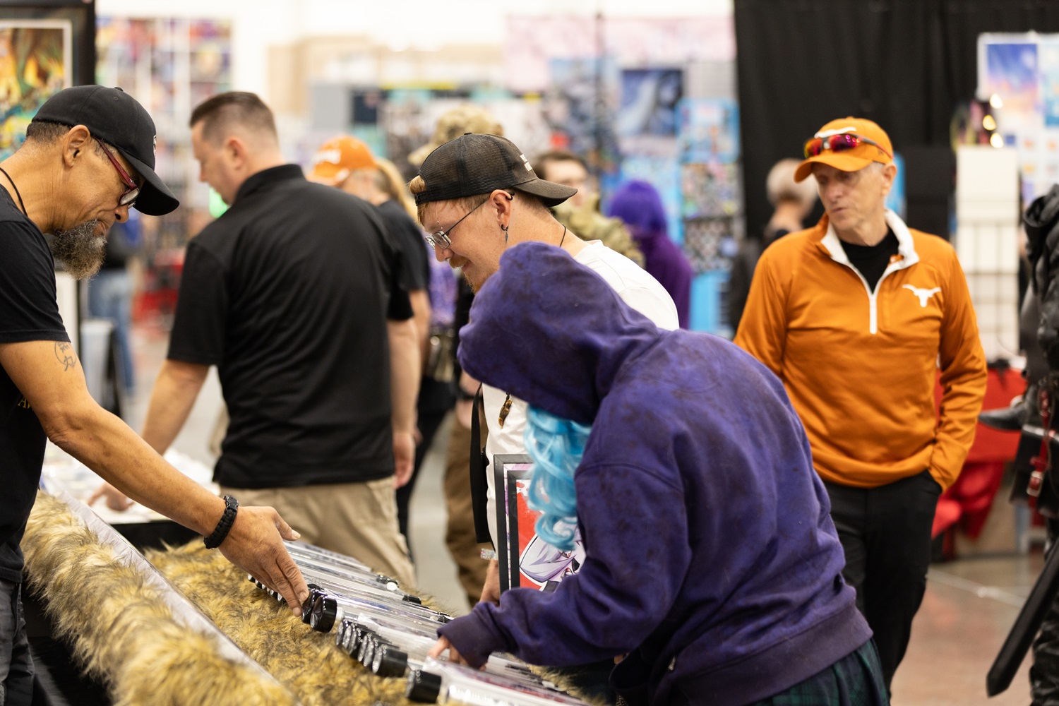 A FAN EXPO attendee inspects a display of swords, engaging with the vendor. Other attendees look on, including a person in a Texas Longhorns jacket.