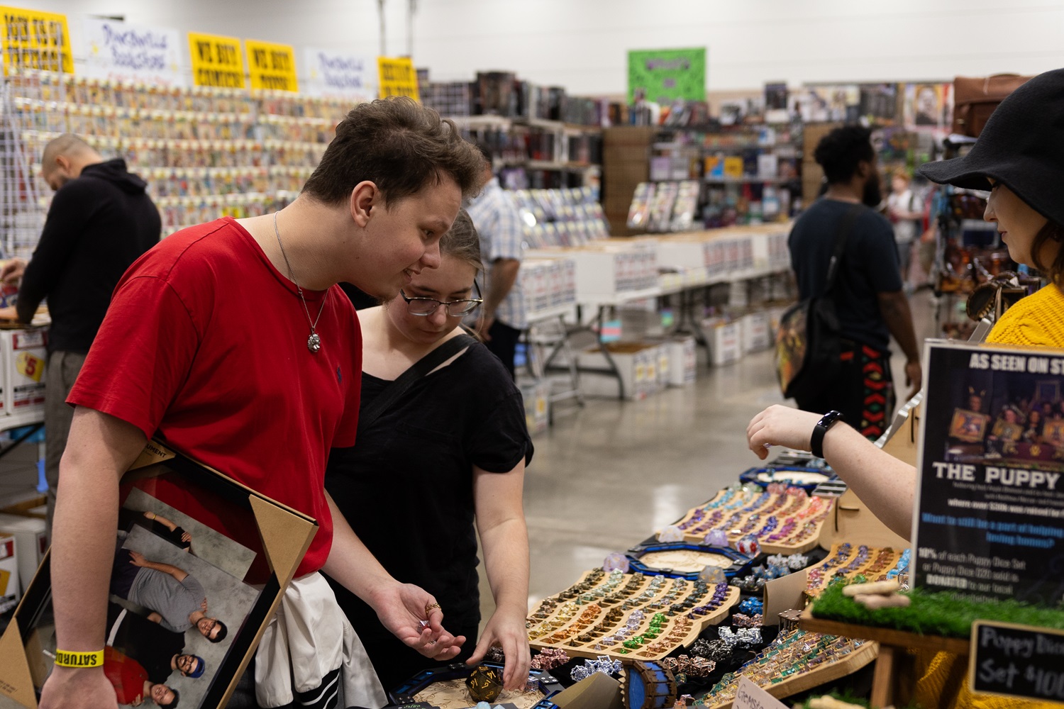 A couple leans over a table covered with various sets of dice, carefully examining the selection with interest at FAN EXPO.