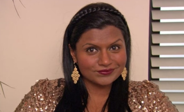 Kelly sits in the interview chair, giving a sassy and knowing look at the camera.