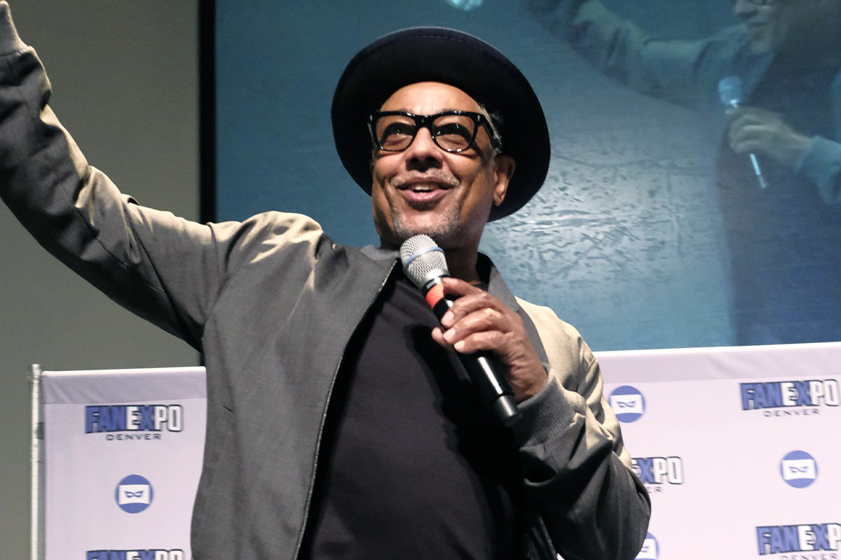 Giancarlo Esposito smiles with his arm extended and other arm holding a microphone
