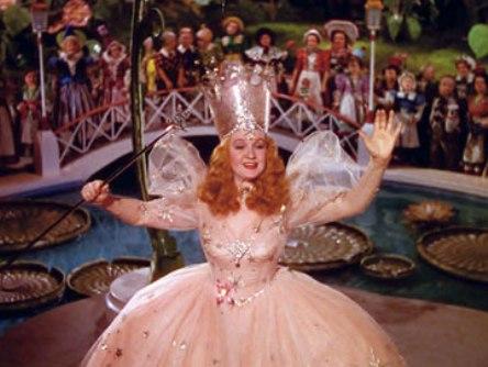 Glinda, in her pink ballgown, waves as she sends Dorothy off down the yellow brick road. Behind her, the residents of Munchkinland see Dorothy off on her adventure.