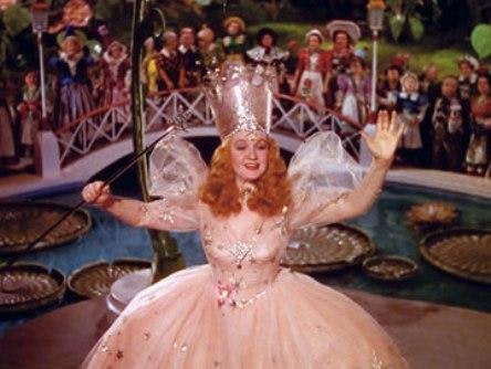 Glinda, in her pink ballgown, waves as she sends Dorothy off down the yellow brick road. Behind her, the residents of Munchkinland see Dorothy off on her adventure.