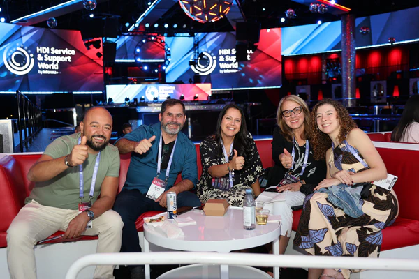 A group of five smiling IT professionals giving a thumbs-up at the HDI Service & Support World conference party, showcasing team building and community networking.