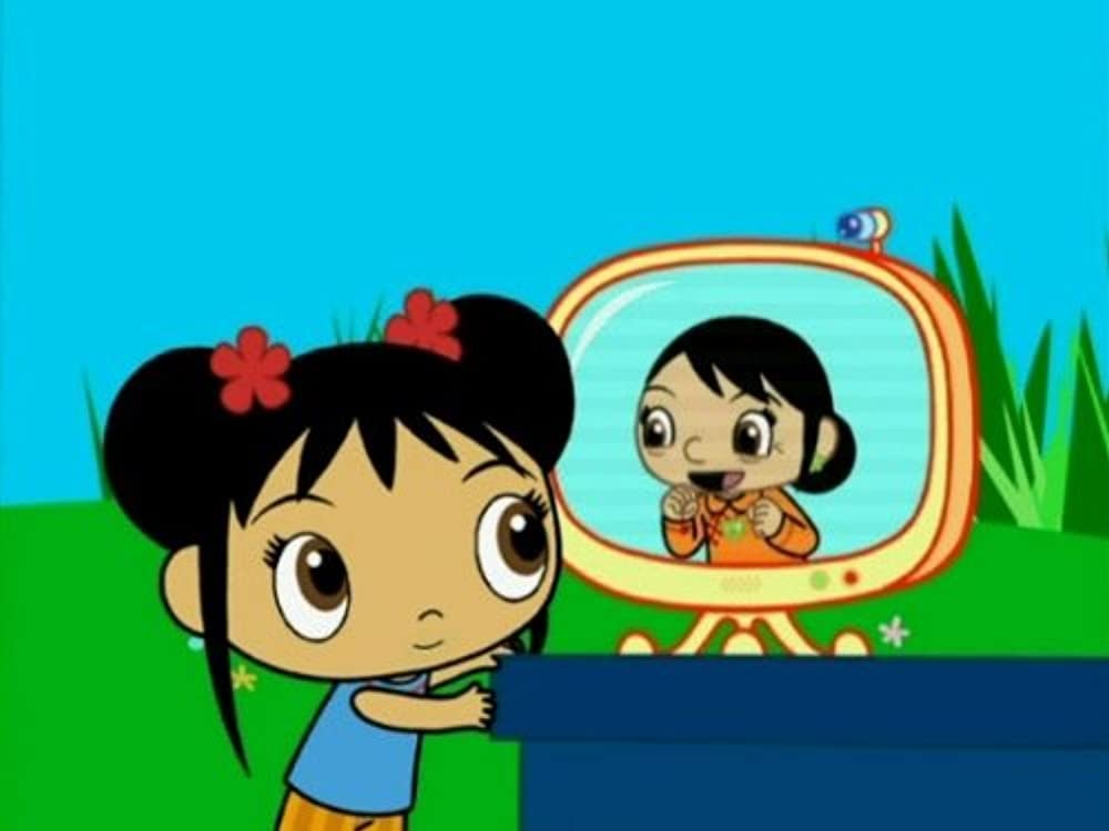 Kai-Lan, wearing a blue shirt, stripped orange pants, and two red flowers in two buns in her black hair. She is turned to the right and looking into a yellow tv screen that us on top of a blue counter. On screen is Gu Nai Nai, who is smiling, wearing an orange shirt and her black hair is in a low bun. Behind them is a grassy hill and blue skies.