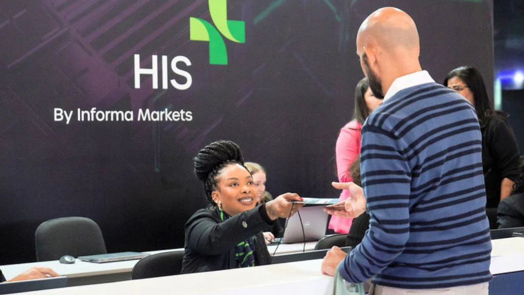 Atendente entregando crachá de identificação para participante no balcão de credenciamento do evento HIS.