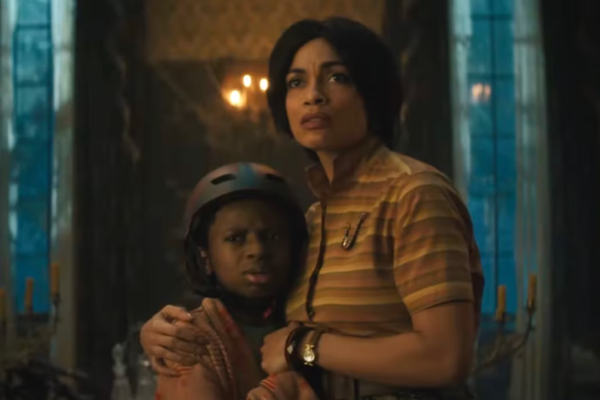 Rosario Dawson in a stripped shirt, hugging a child in a helmet. Both look scared.