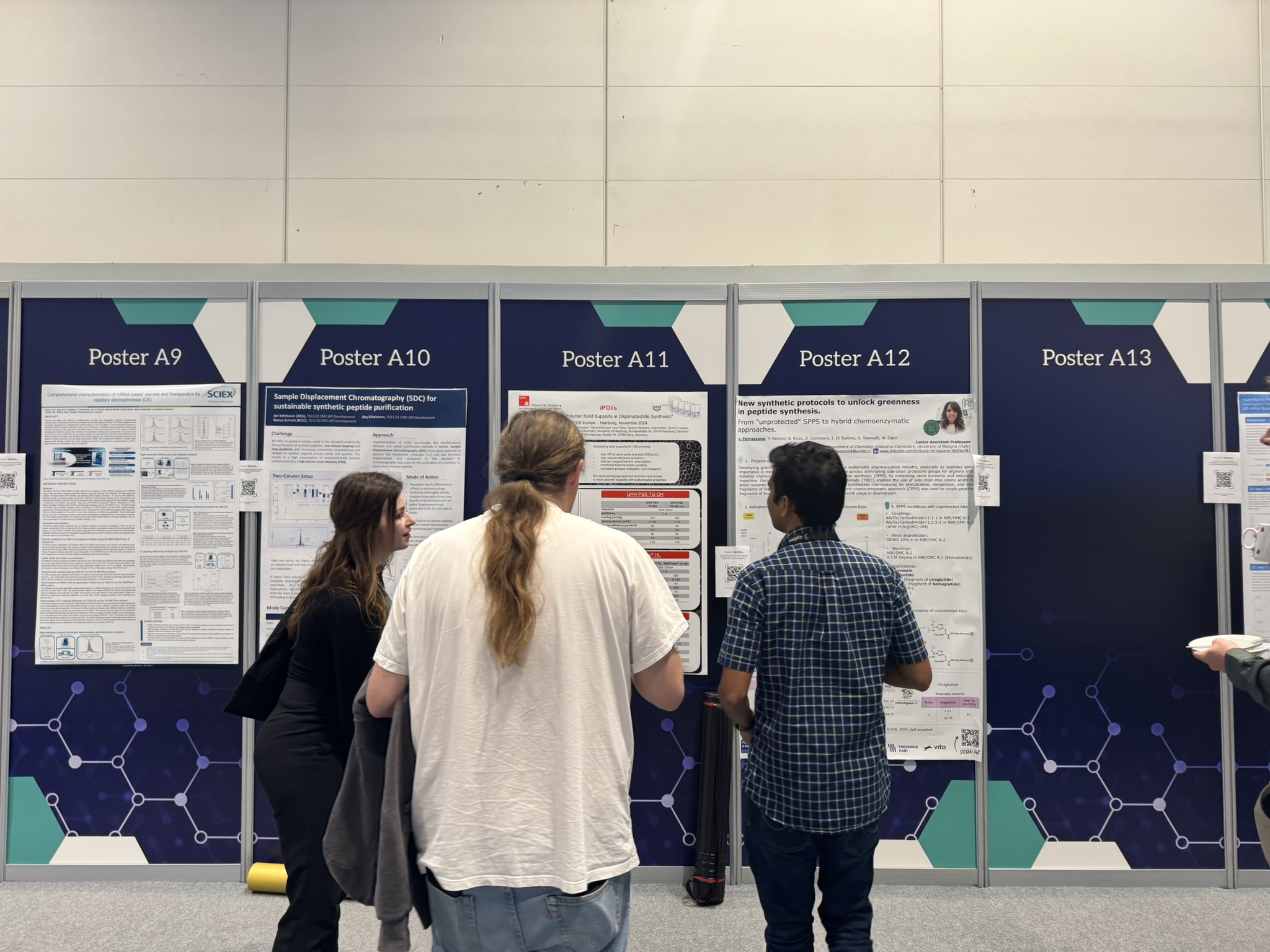 Three people browse a poster wall at TIDES Europe