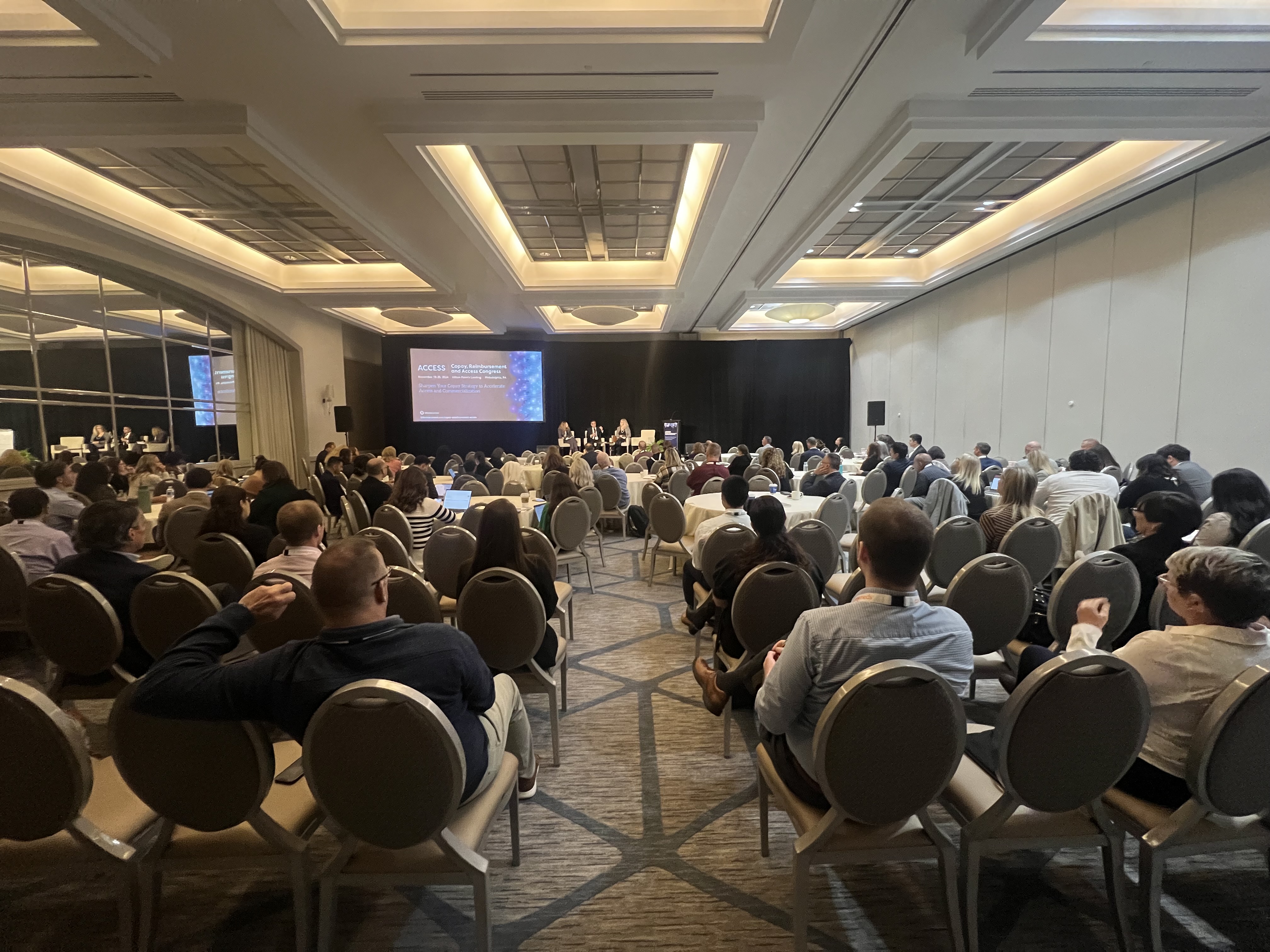 Pharma professionals fill a session room while access experts deliver a panel discussion