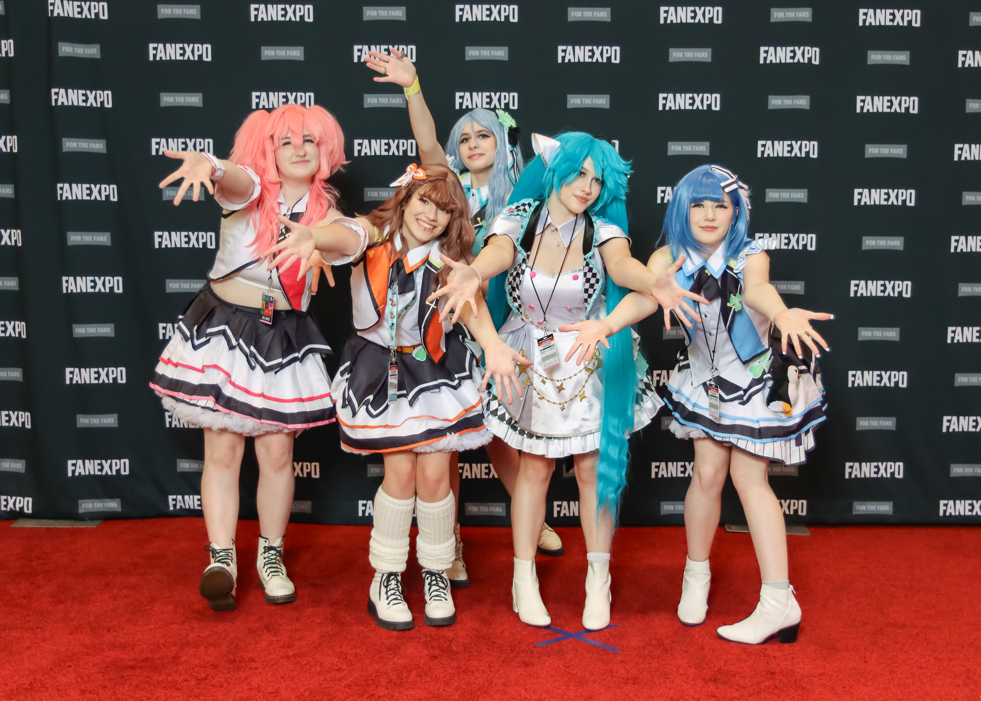 The image displays a group of individuals posing on a red carpet against a backdrop with the text "FAN EXPO," indicative of a fan convention. Each person is in a costume that reflects a character from a maid anime show. they are posing with their hands outstretched and leaning forwards.
