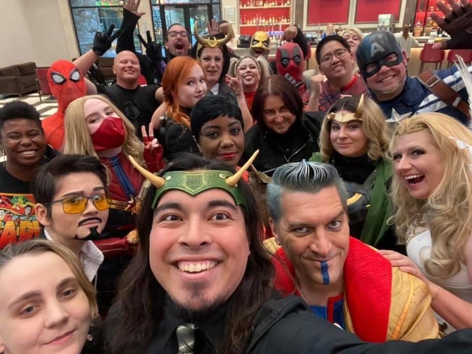 A large group of cosplayers taking a cheerful selfie. The group features characters like Loki, Captain America, Spider-Man, and various other Marvel heroes, creating a fun and energetic snapshot of fandom camaraderie.
