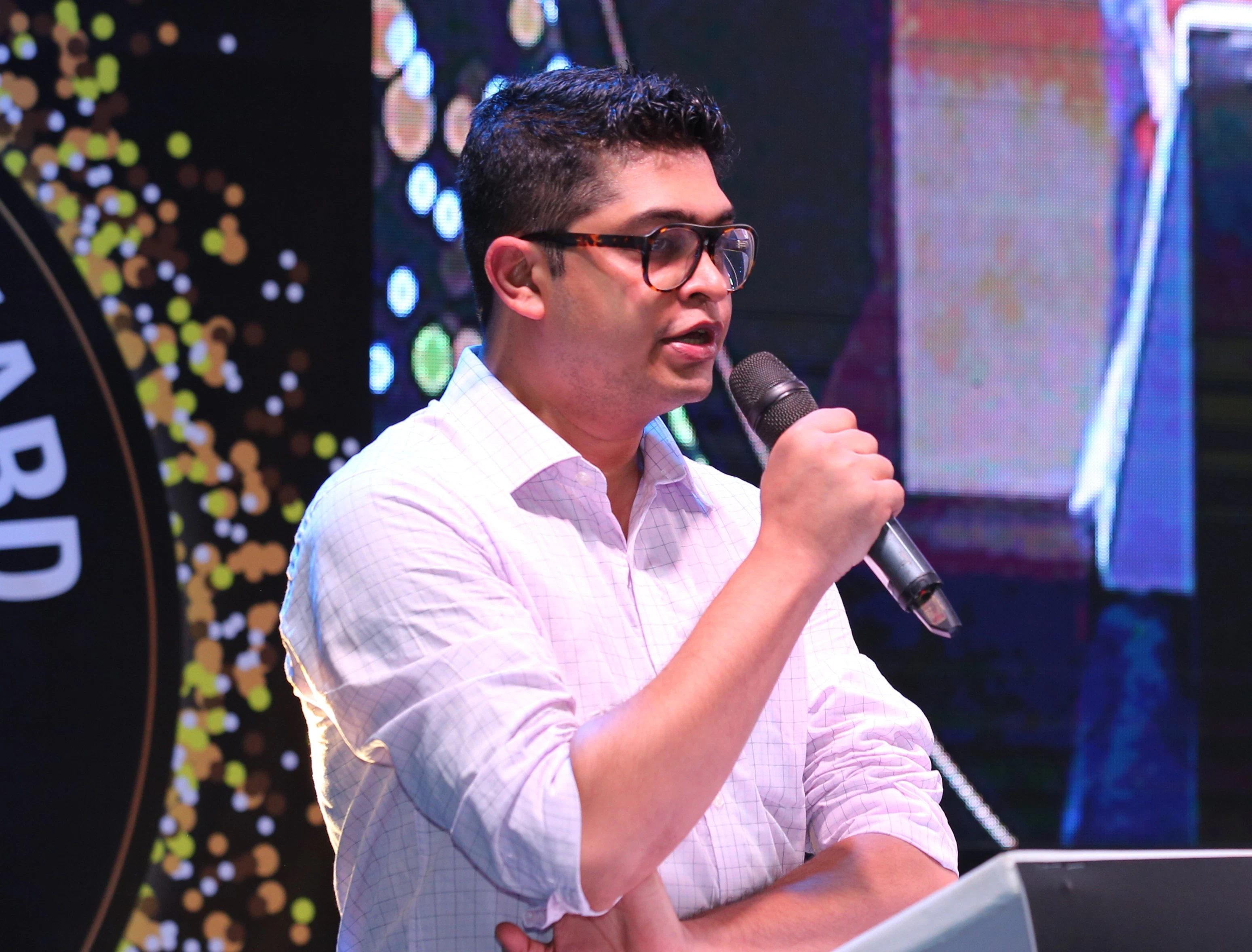 Man wearing glasses and a shirt speaking at a podium during the IRAA Palm Awards