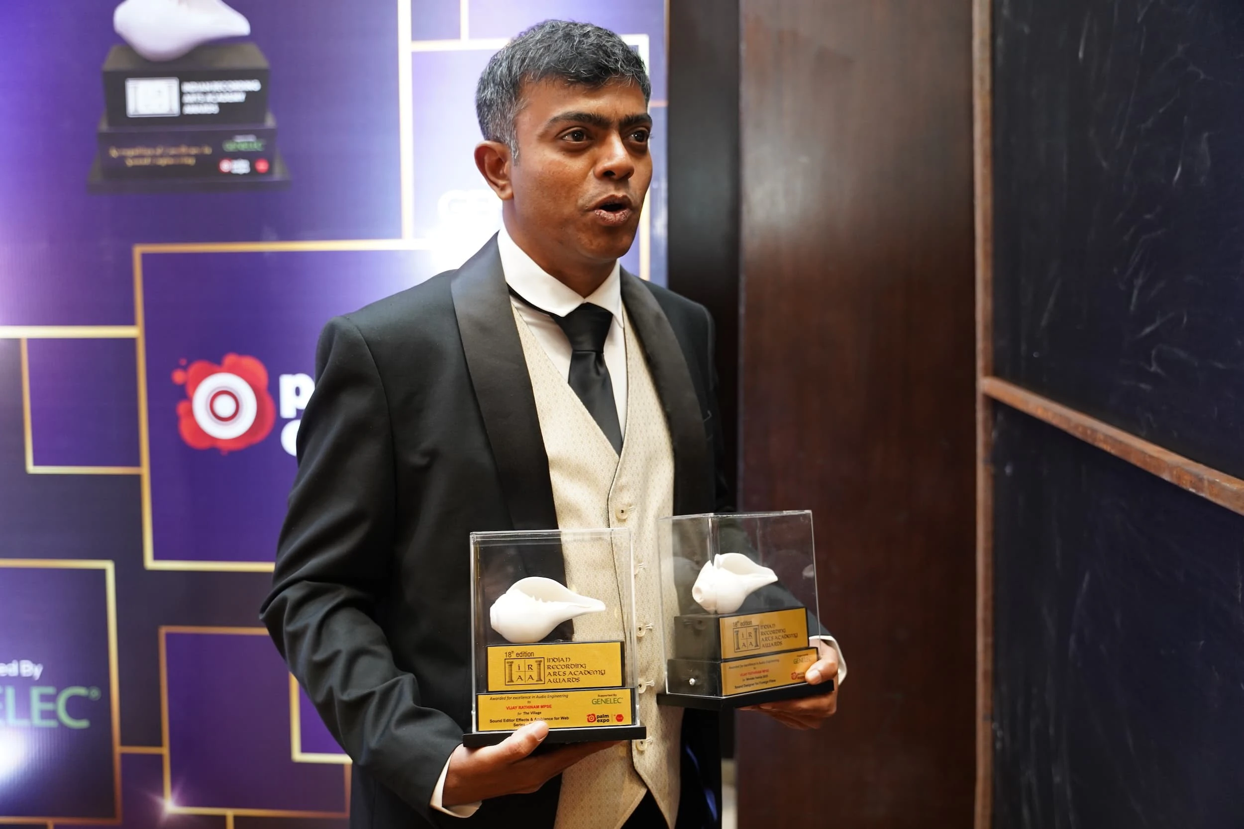 Man in a formal suit happily holding two awards at the IRAA Palm Awards Image 5 - Three people conversing casually in the lounge area of the IRAA Palm Awards
