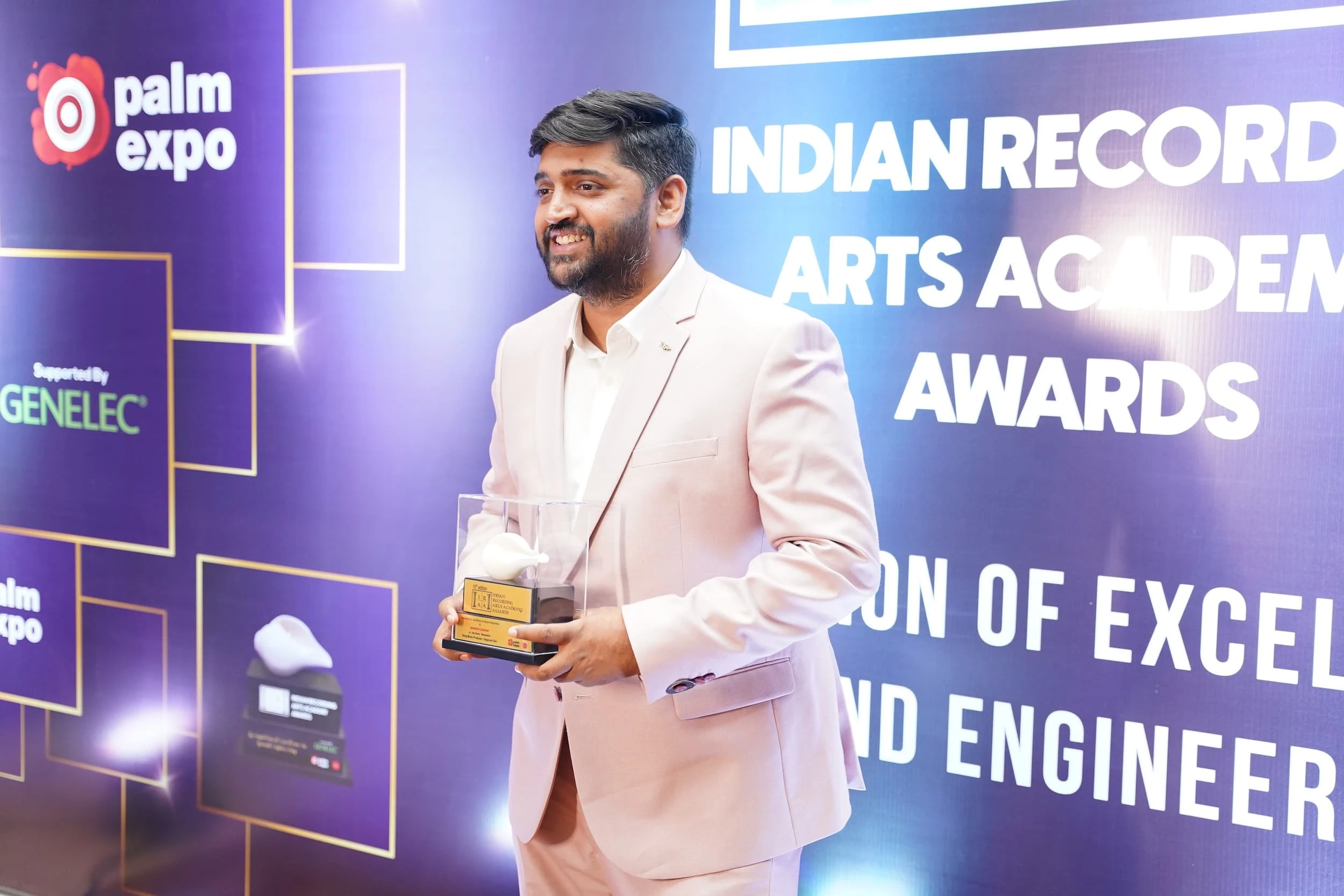 Man in a light suit holding an award in front of the IRAA Palm Awards branded backdrop