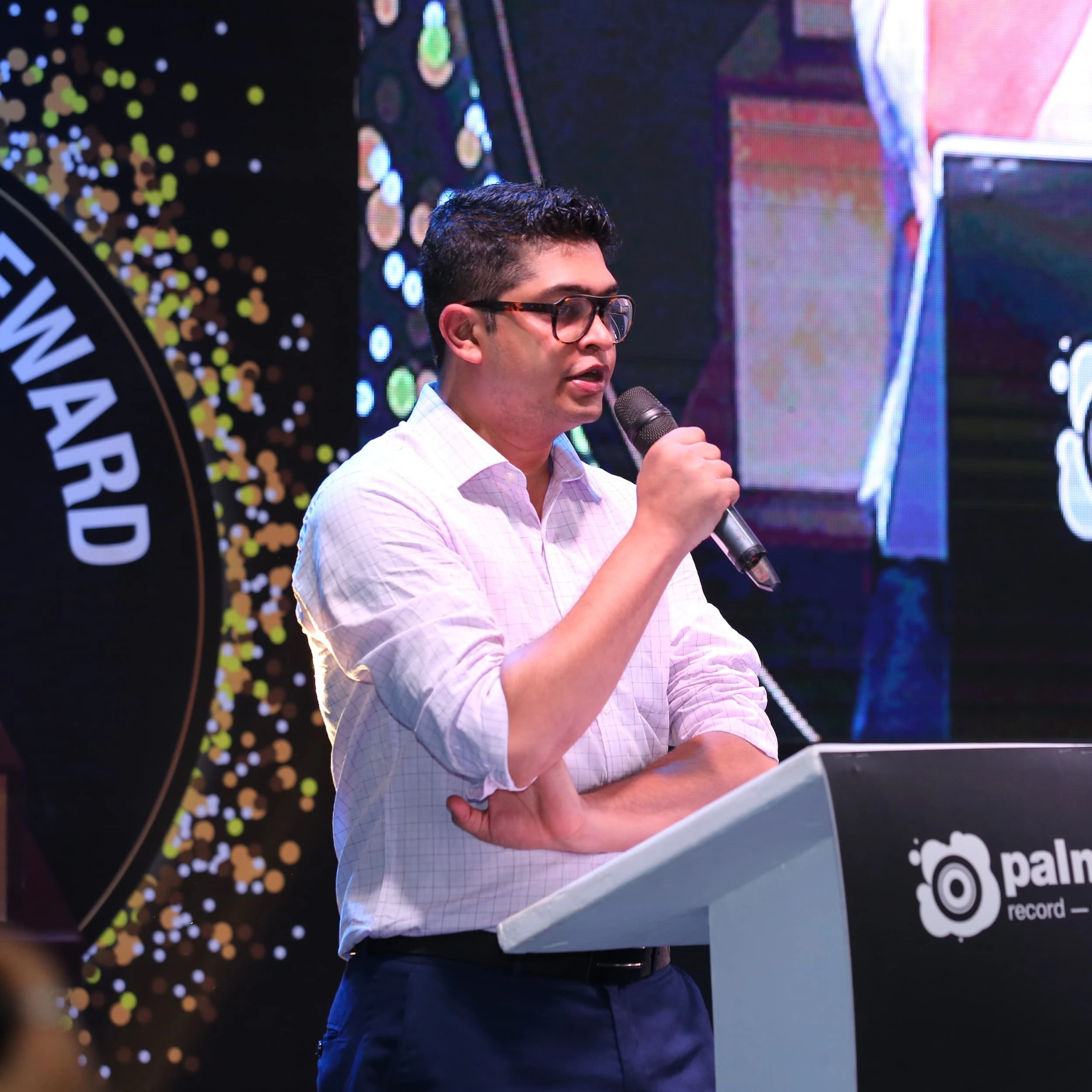 Man wearing glasses and a shirt speaking at a podium during the IRAA Palm Awards