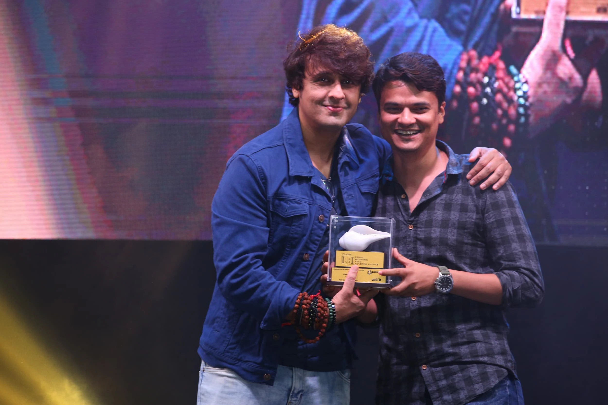 Two men posing together on stage while holding a trophy at the IRAA Palm Awards
