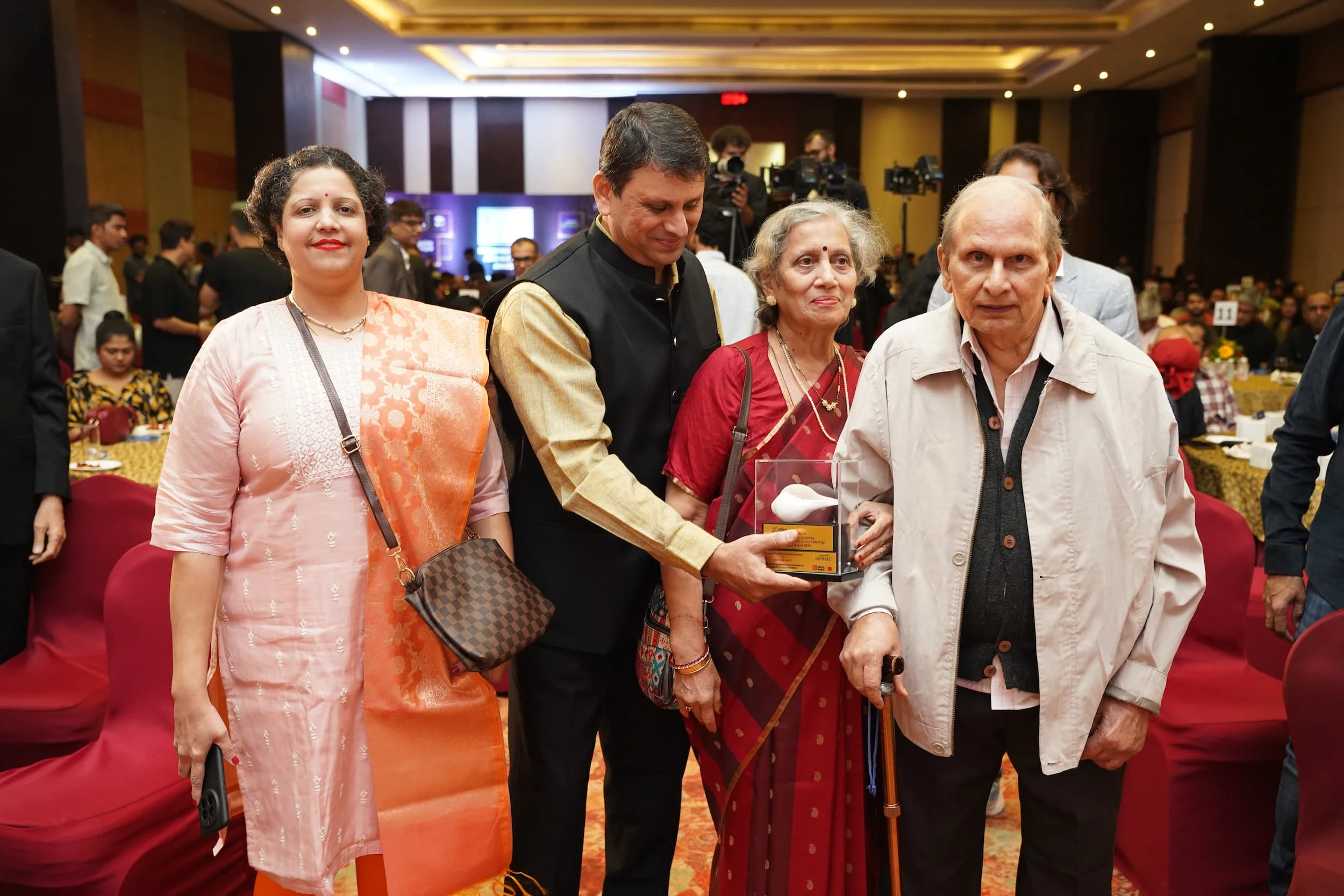 Four people posing together at the IRAA Palm Awards, with the award presented to the eldest person on the left.